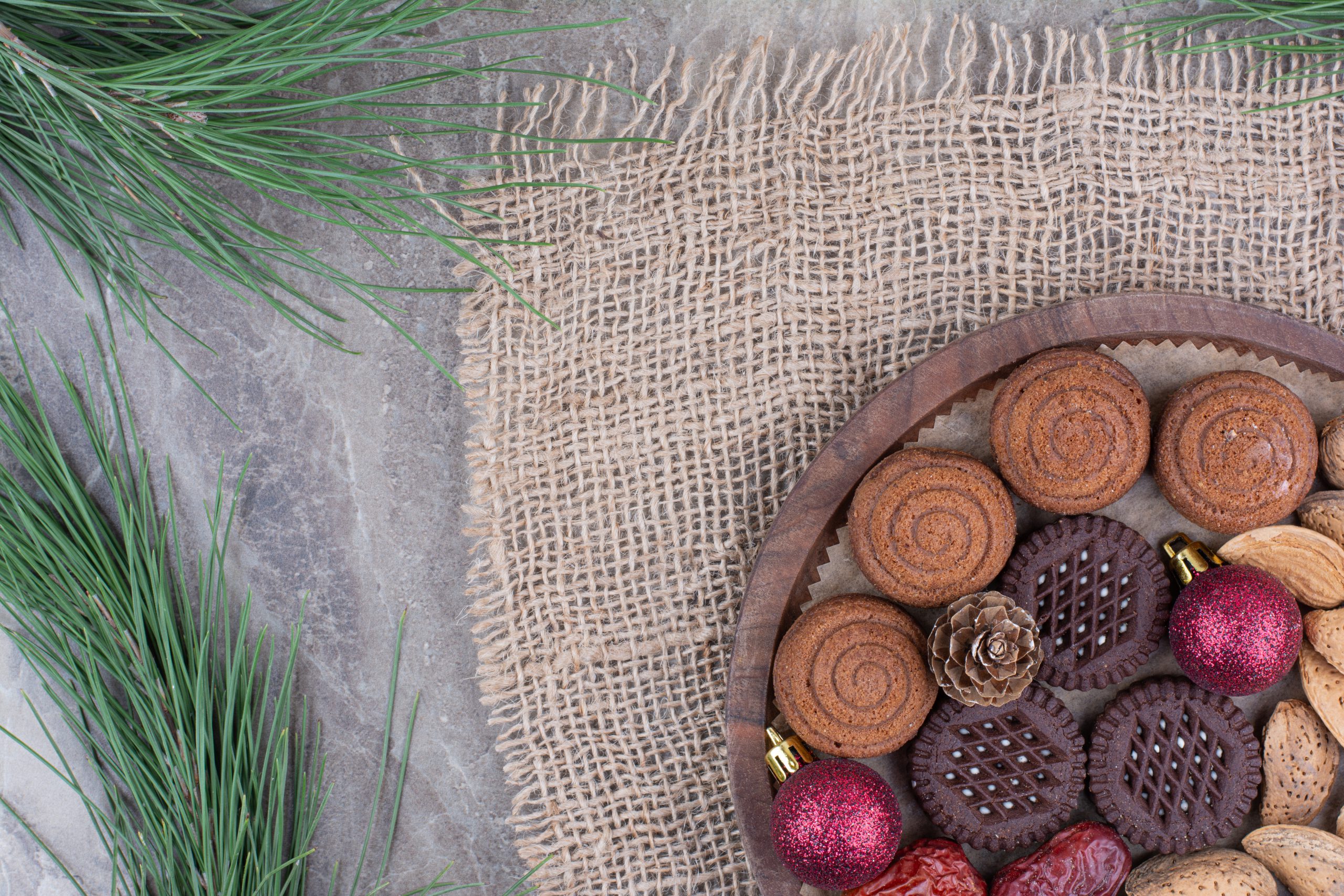 Czekoladki świąteczne i ciasteczka na drewnianej paterze w świątecznej aranżacji z gałązkami sosny
